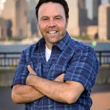 A man with his arms crossed in front of a city skyline.