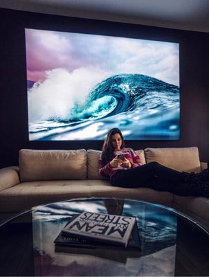A woman sitting on a couch in front of a backlit wall art hanging of a beautiful wave