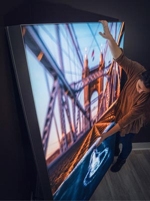 A woman examining a backlit wall art hanging of a bridge structure