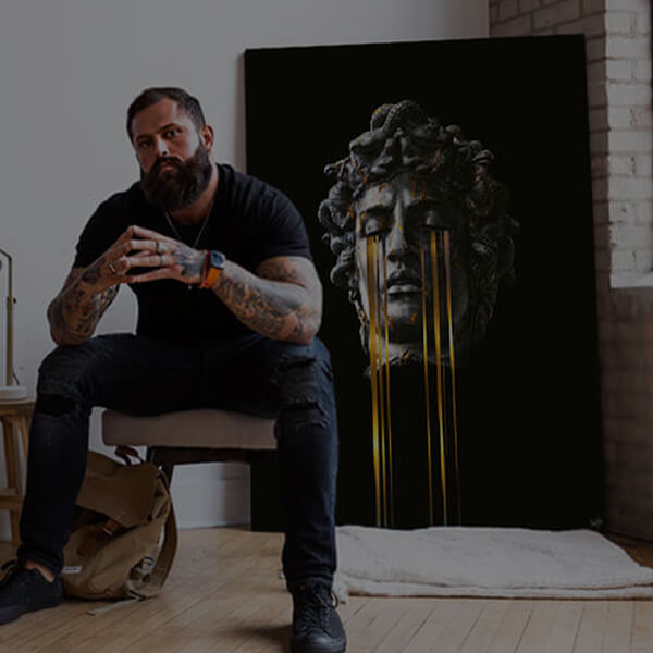 man sitting in front of a painting of a statue with yellow tears streaming from its eyes.