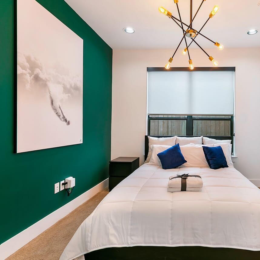 Oversized neutral wall art hung on jade green accent wall in otherwise white bedroom