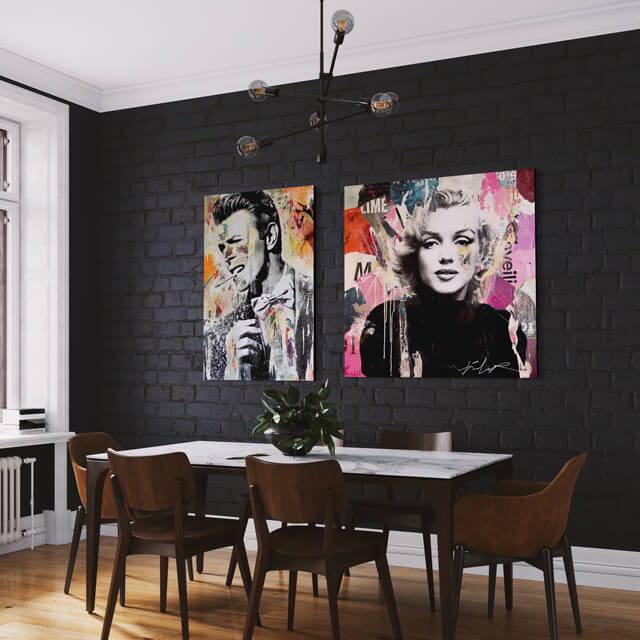 Two pop art photos hang side by side on black painted brick wall in city apartment dining room. Each large pop artwork shows a celebrity in black and white surrounded by a colorful collage.