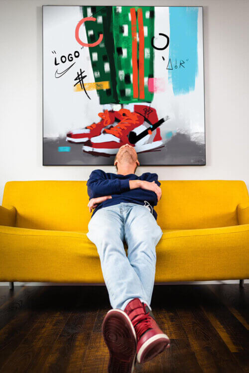 Pop sneaker wall art featuring painted red Air Jordans hangs above yellow couch with man wearing red Air Jordan Sneakers