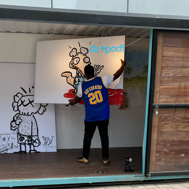 Artist Stephen Smith hangs his ArtPrize 2022 entry "Ugly Clothes" which are 3 digitally drawn characters in black and white printed on BIG Wall Décor in His Art Pod