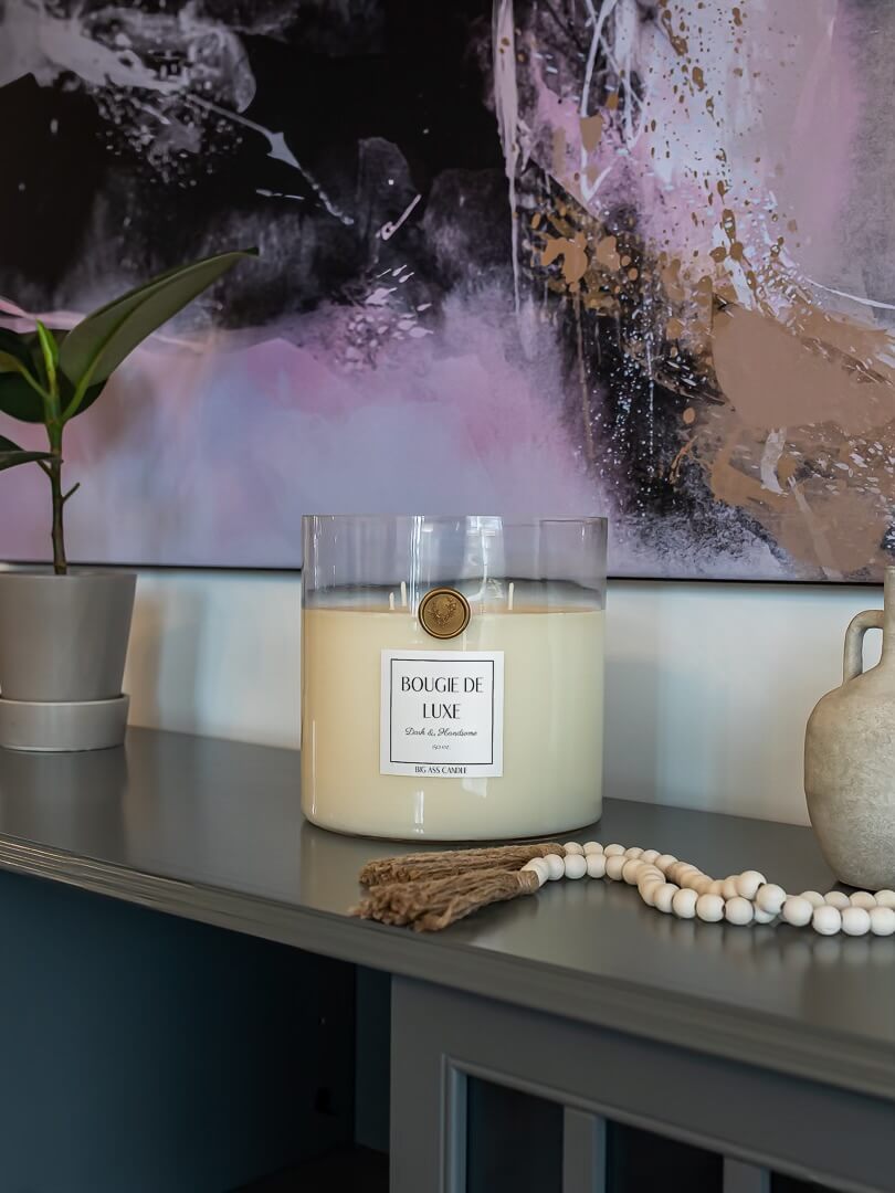 Large candle from big ass luxuries sits on blue grey counter next to indoor house plant and two ceramic vases below a big ass wall art from BIG wall décor