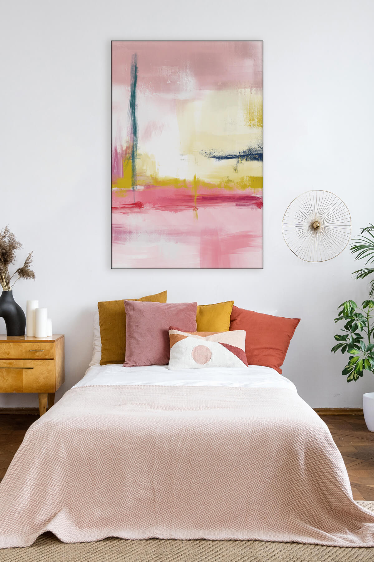 A light pink and yellow abstract artwork is hanging above a little girl's bed which is covered with a light pink duvet and several pink and yellow throw pillows. The artwork features shades of pink from light to dark mixed with mustard yellow and one accent of navy blue, adding a playful and vibrant touch to the room's décor.