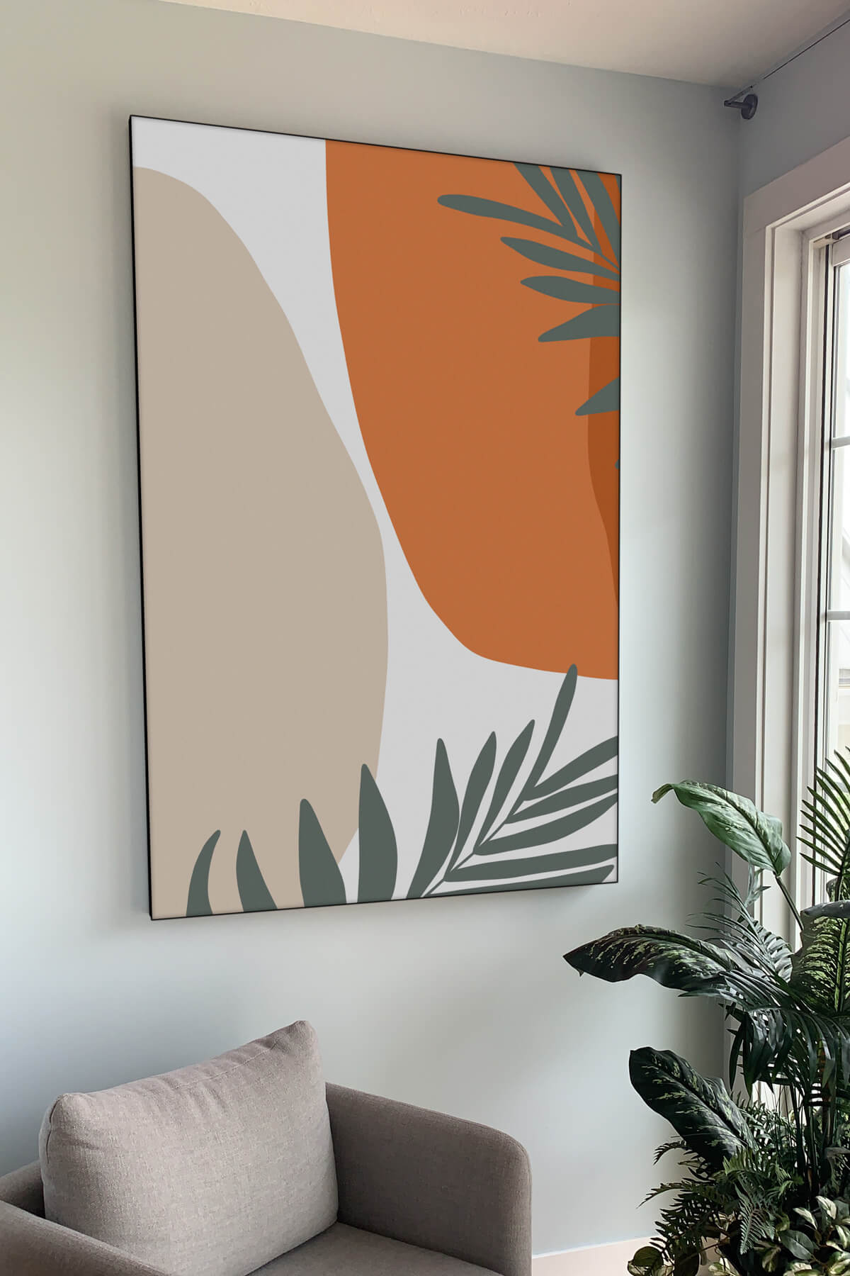 Extra large orange and tan abstract art with sage green tropical leaves hangs on white living room wall.