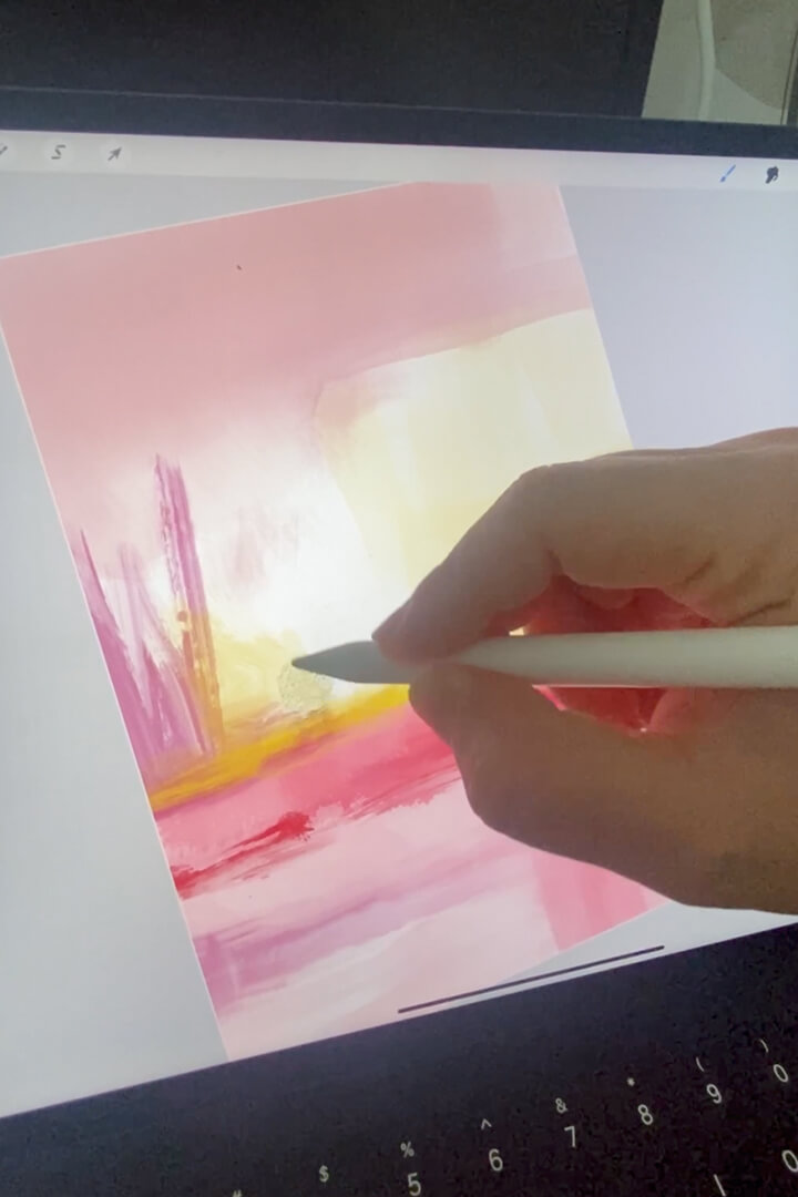 Close-up shot of abstract artist Karine Tonial Grimm's hand holding a white Apple pen and adding yellow to a pink abstract artwork on an iPad. The artist's precise movements can be seen as she creates her piece