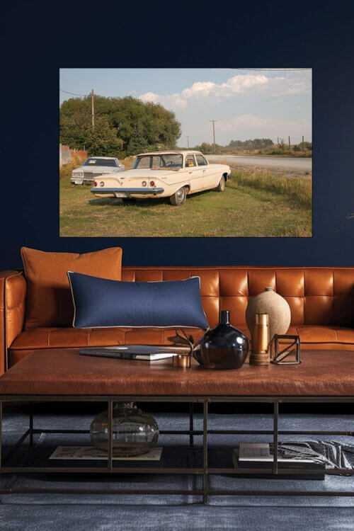 Large vintage car wall decor in cream green and blue hangs above leather couch on navy blue wall in guys living room.