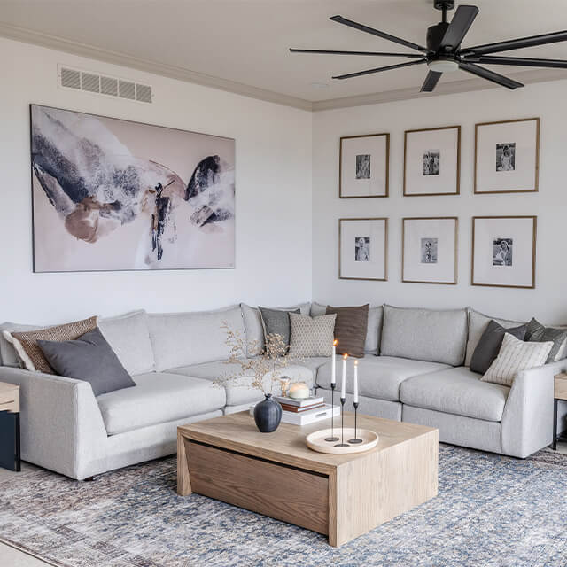 A large abstract painting above a sectional sofa and a gallery wall of six framed photos in a modern living room, illustrating how to choose the right wall art size.