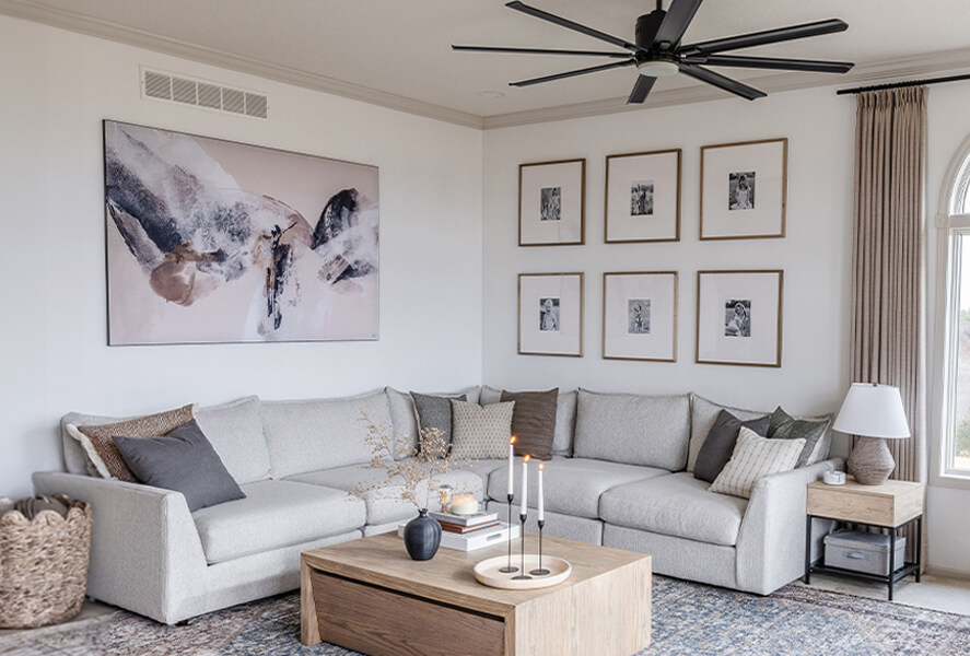 A modern living room featuring a large abstract painting above a sectional sofa and a gallery wall of six framed photos, illustrating how to choose the right wall art size.