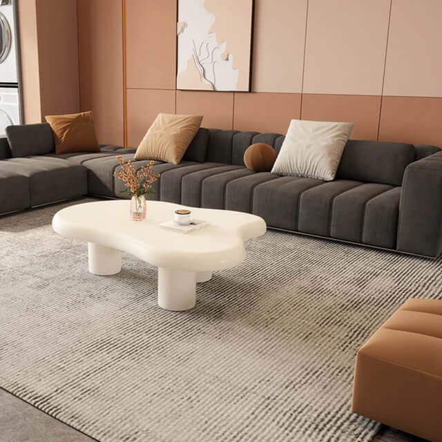 Contemporary gray sectional sofa in a peach-toned room with layered textures, plush pillows, and rounded furnishings.