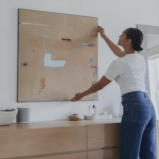 Woman holding neutral brown 48"x48" abstract square big wall decor print over a dresser and smiling.