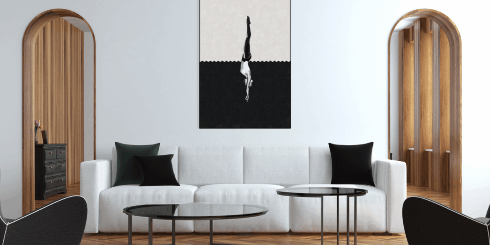 Modern living room with a white sofa, black and green pillows, glass coffee tables, and a geometric black and white artwork of a diver on the wall.