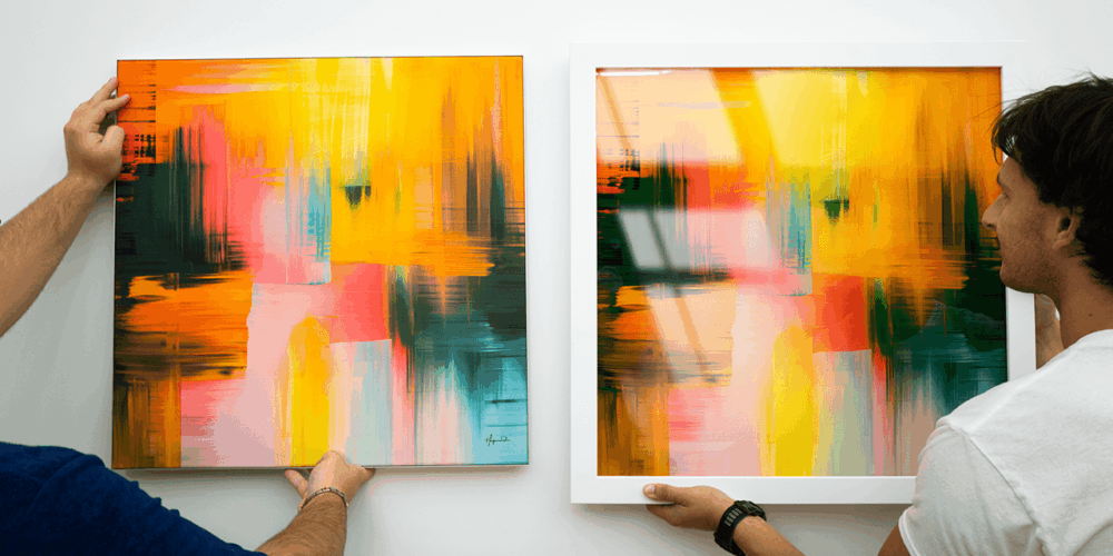 Two people compare two prints. One is artfab fabric print with infinity frame the other is infused acrylic wall art prints of a bold abstract painting with yellow, pink, green, and orange brushstrokes in a white Bonanza wood frame.