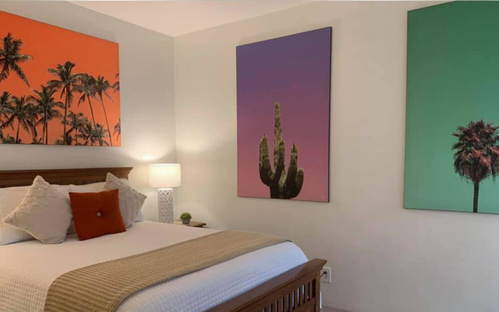 Colorful palm tree wall art featuring palm trees and cactus on colorful backgrounds decorate the walls in neutral bedroom.
