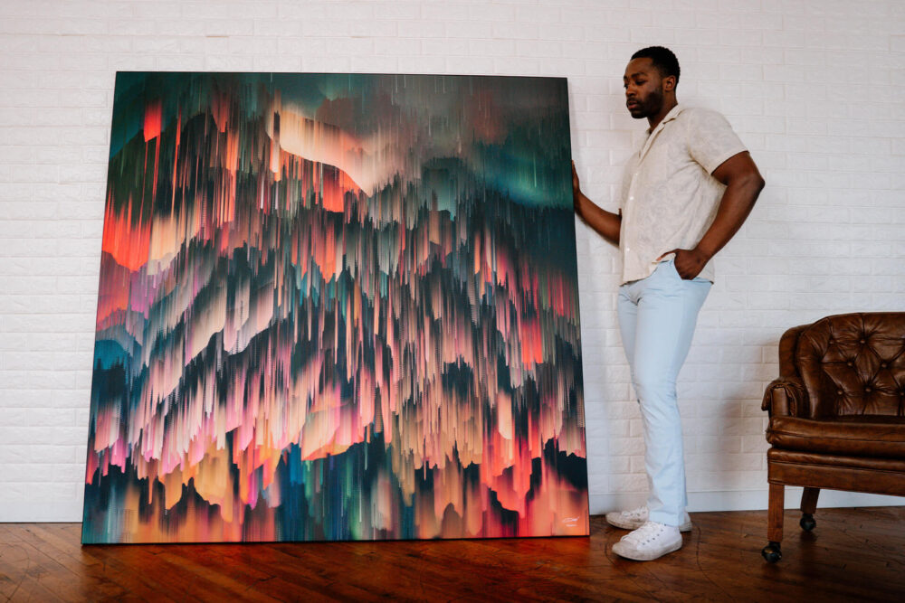 Extra large square colorful abstract art showing colors falling from the sky leans on white wall next to man