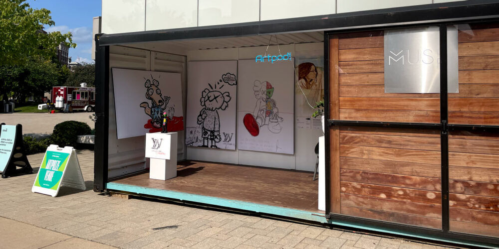 The Art Pod Venue at ArtPrize 2022 holds two exhibits. The one shown is three massive black and white prints of digitally drawn characters wearing branded clothes. Text on the prints makes you wonder about your value and identity.