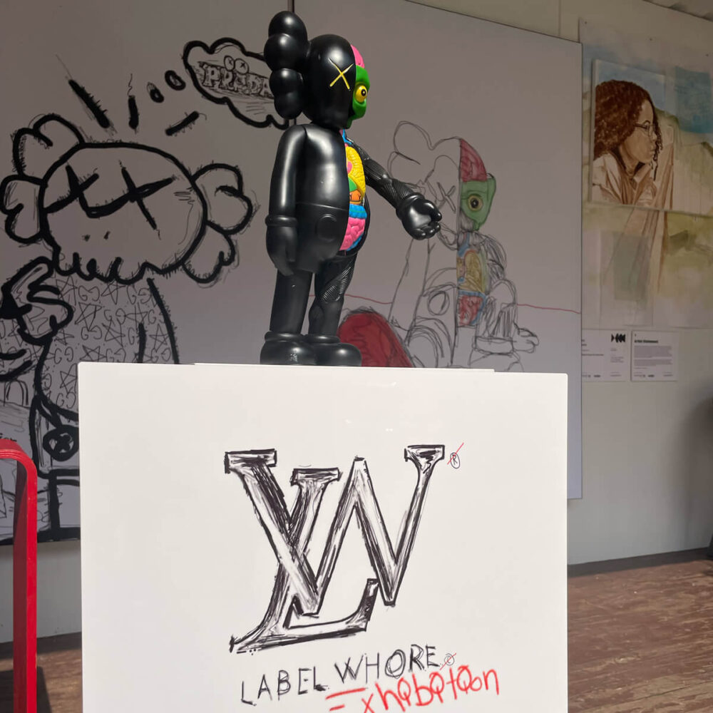 Gloss Metal Print hung with black and white "Label Whore" logo for the "Ugly Clothes" exhibit, which looks like the Louis Vuitton logo.