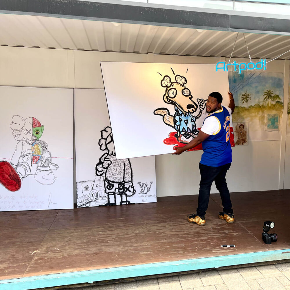 Artist Stephen Smith hangs his ArtPrize 2022 entry "Ugly Clothes" which are 3 digitally drawn characters in black and white printed on BIG Wall Décor in His Art Pod