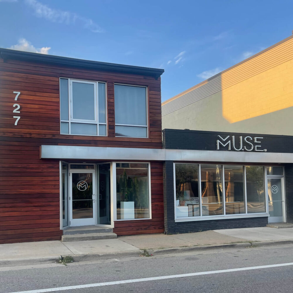 Muse GR Art Gallery has a newly updated exterior with dark stained wood paneling, big glass windows, and dark gray painted siding.