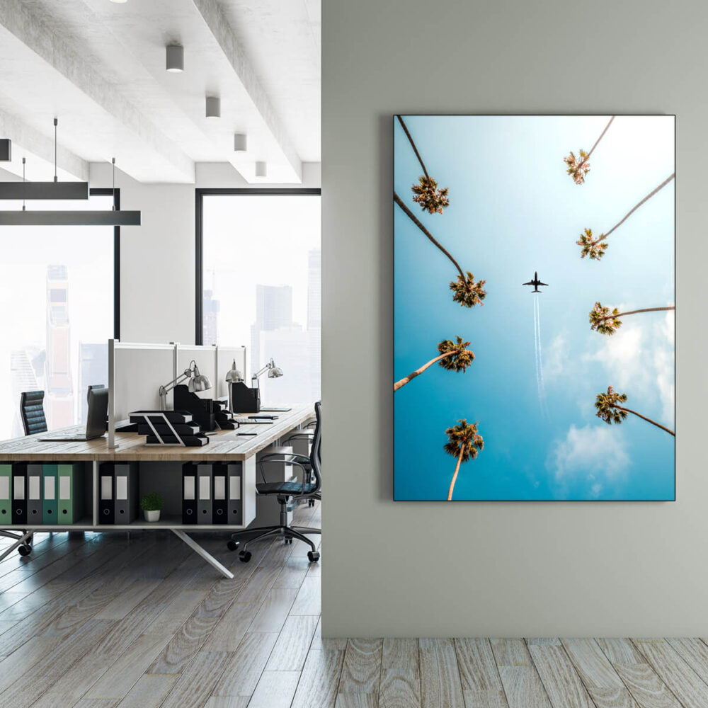 Large Palm Tree wall art with blue sky hangs on gray wall in office building next to cluster of desks