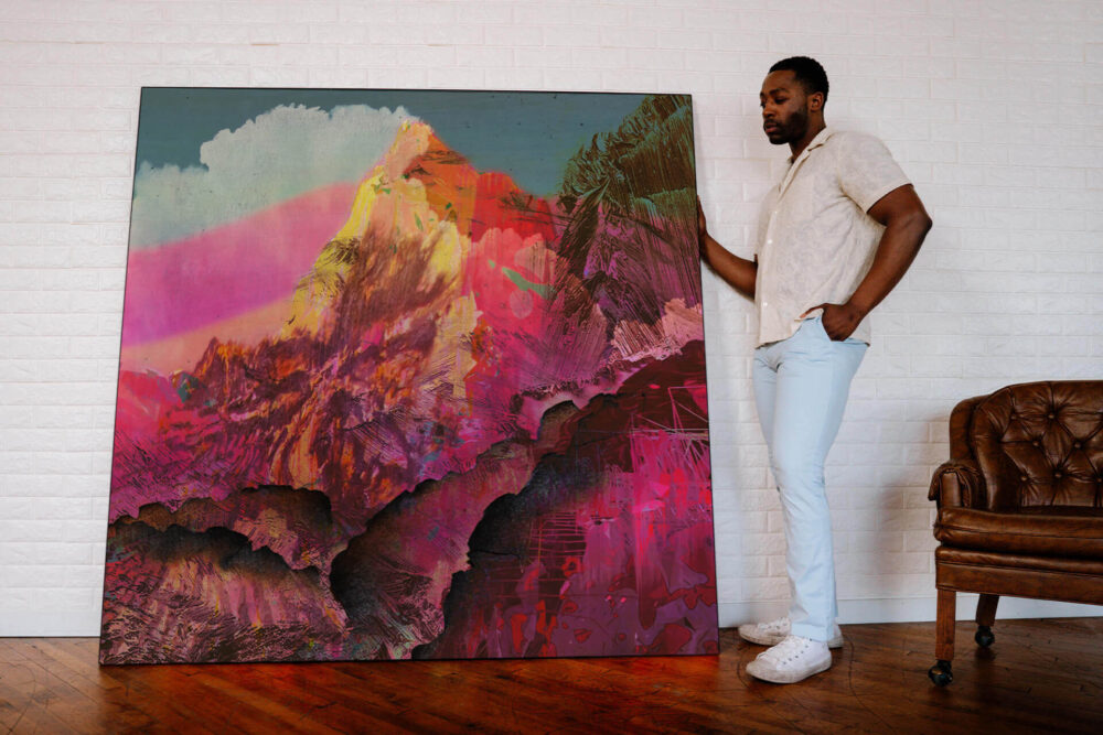 Oversized pink abstract artwork of mountain landscape leans up against white brick wall with man standing next to artwork