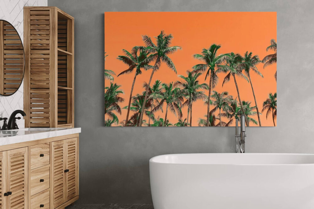Extra large colorful bathroom wall art with palm trees on orange background hangs on light grey wall above soaking tub in bathroom.