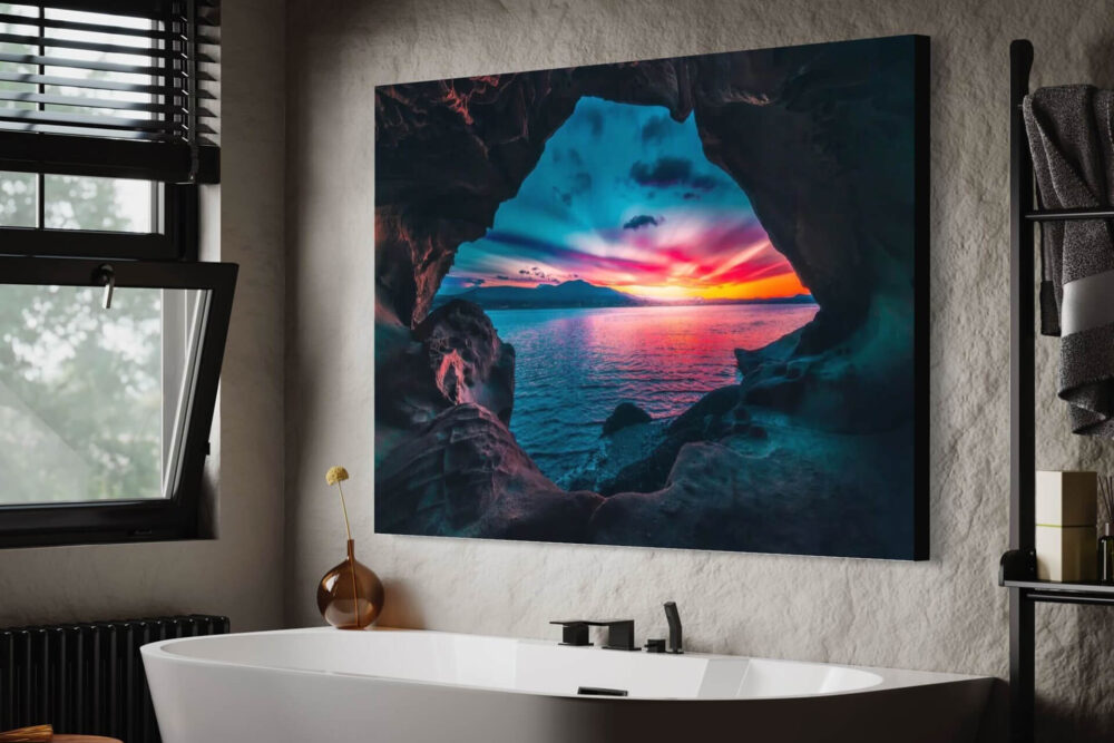 Vibrant sunset photo shot through rock cove hangs on wall in modern white bathroom.