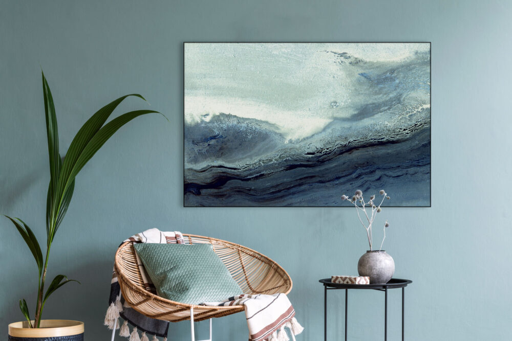 Blue neutral abstract wave art hangs on coordinating blue wall above wicker chair in living room.