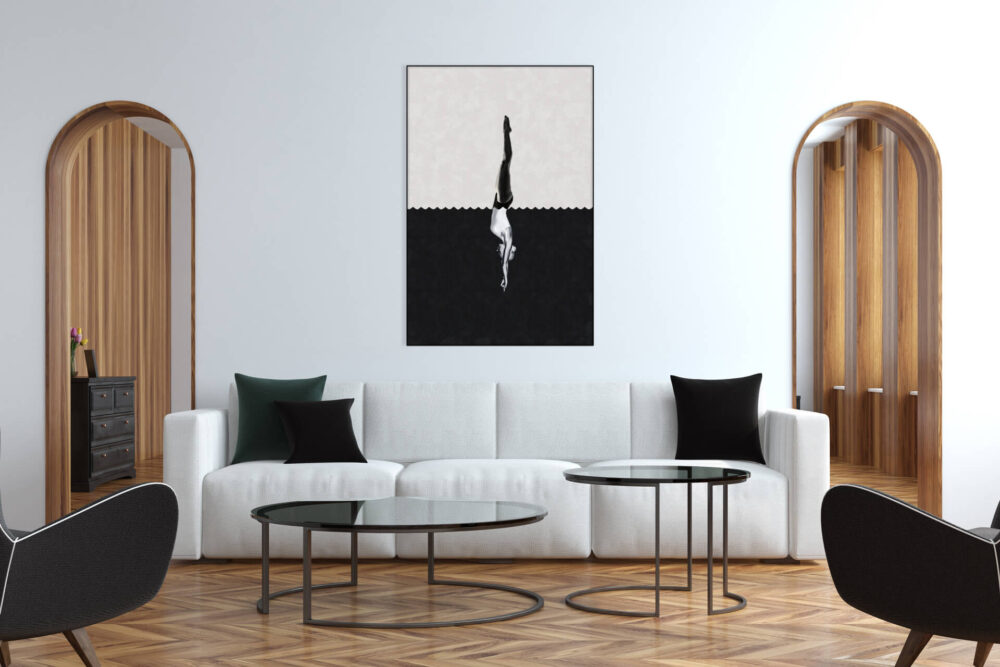 Black and white surreal art showing a person diving from white to black hangs on living room wall above white couch.