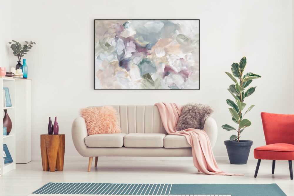 Large pastel floral abstract painting hangs above tan couch decorated with pink throw pillows and blankets in feminine living room.