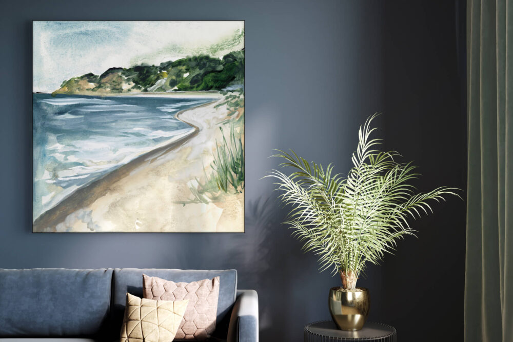 Square watercolor painting of Lake Michigan beach hangs on blue wall above a couch next to a side table adorned with vase filled with fluffy palm fronds.