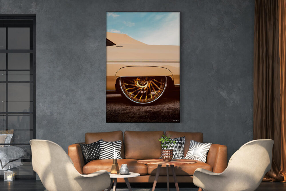 Vertical photo of car wheel featuring gold shiny rims hangs on neutral gray wall above a leather couch in a living room decorated for spring.