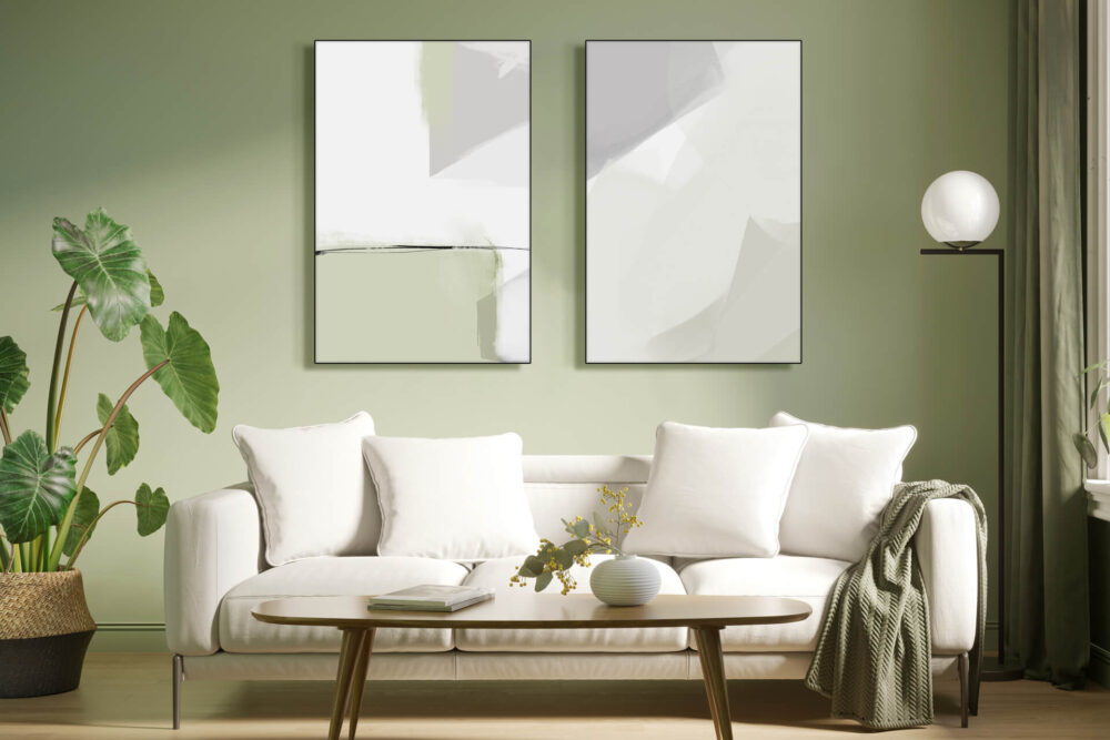 Two light sage green and white minimal pieces of art hang side by side on sage green wall above white couch in living room.