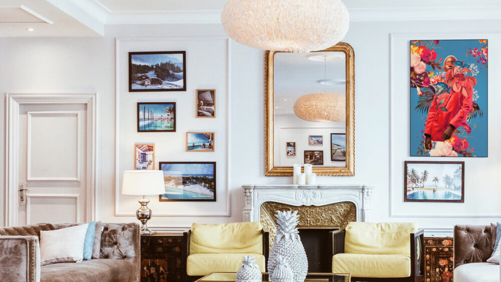 Vintage maximalist living room with yellow antique chairs, a vintage mirror above an ornate gold and white fireplace, and a gallery wall featuring an eclectic collection of frames and "All the Springs She Remembered" by Frank Moth, a colorful maximalist wall art piece.