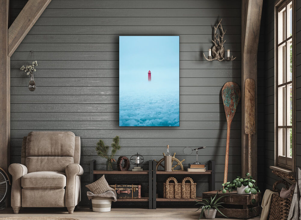 Large landscape photography of a foggy light house mostly light blue with a pop of glimpse of the red light house hangs in a living space