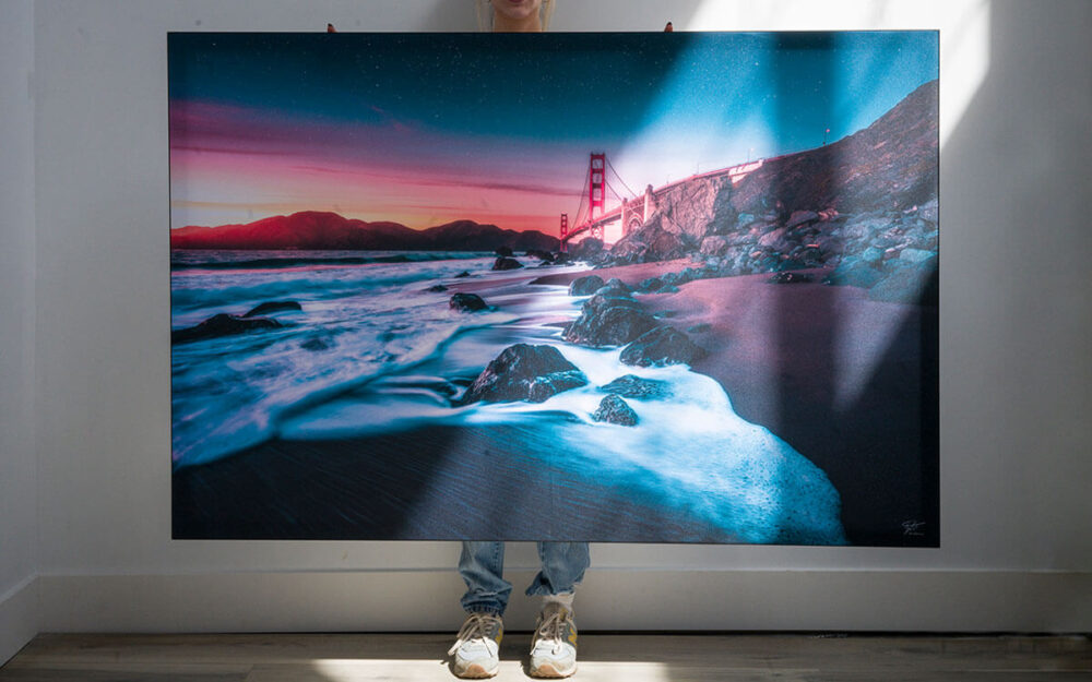 Colorful nature photo printed as large custom wall art being held by girl in living room with white walls.