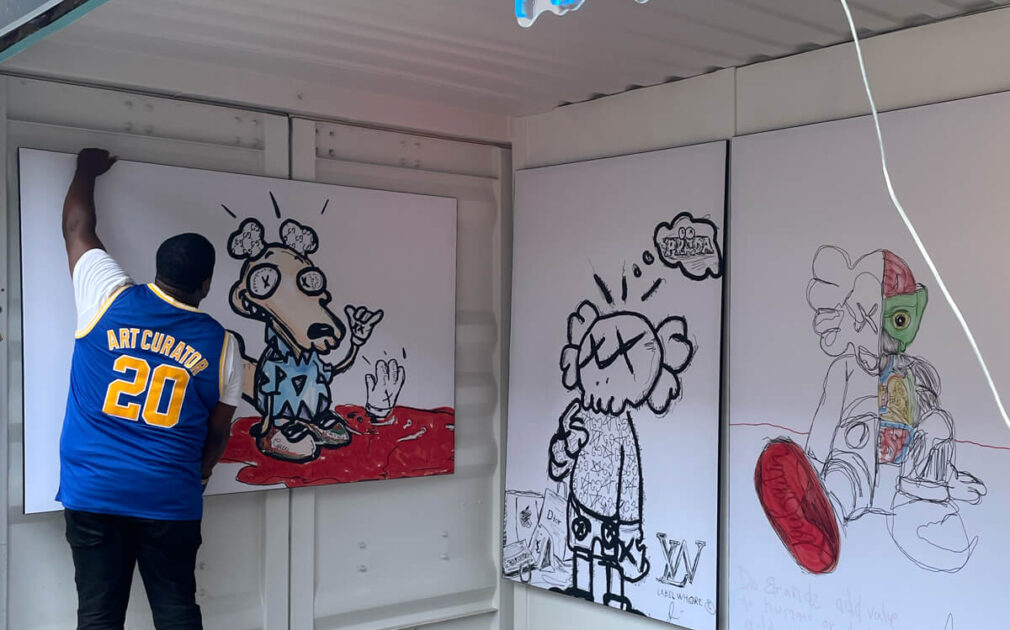 Artist Stephen Smith hangs his ArtPrize 2022 entry "Ugly Clothes" which are 3 digitally drawn characters in black and white printed on BIG Wall Décor in His Art Pod