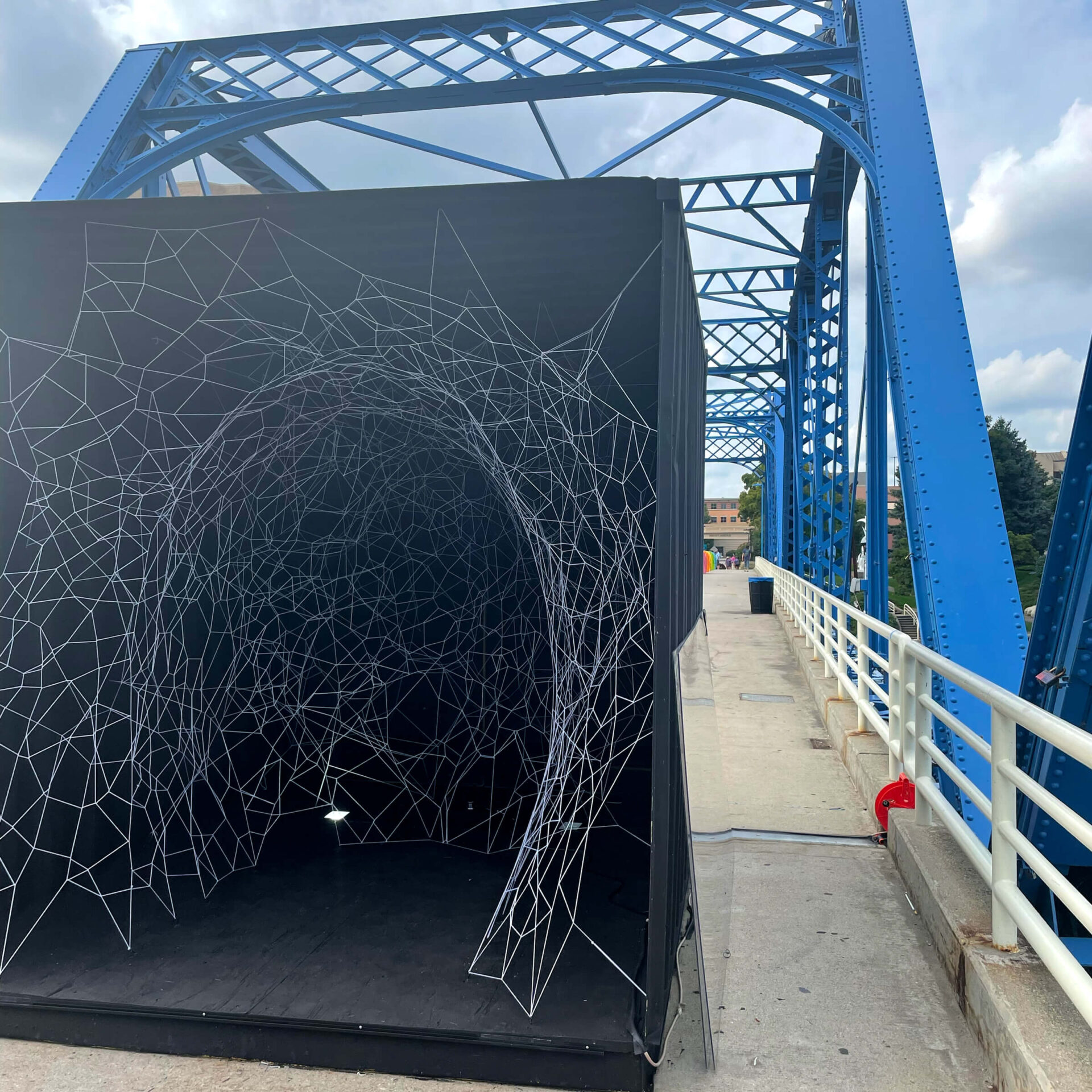 Dark container filled with web of netting displayed on Blue Bridge in Grand Rapids for ArtPrize 2022