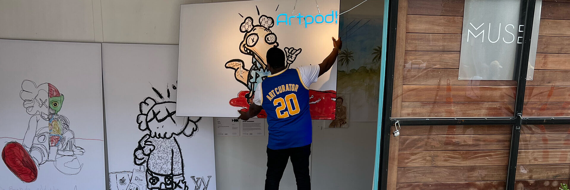 Artist Stephen Smith hangs his ArtPrize 2022 entry "Ugly Clothes" which are 3 digitally drawn characters in black and white printed on BIG Wall Décor in His Art Pod