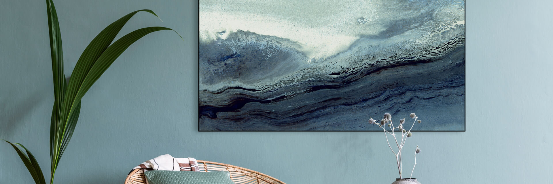 Blue neutral abstract wave art hangs on coordinating blue wall above wicker chair in living room.