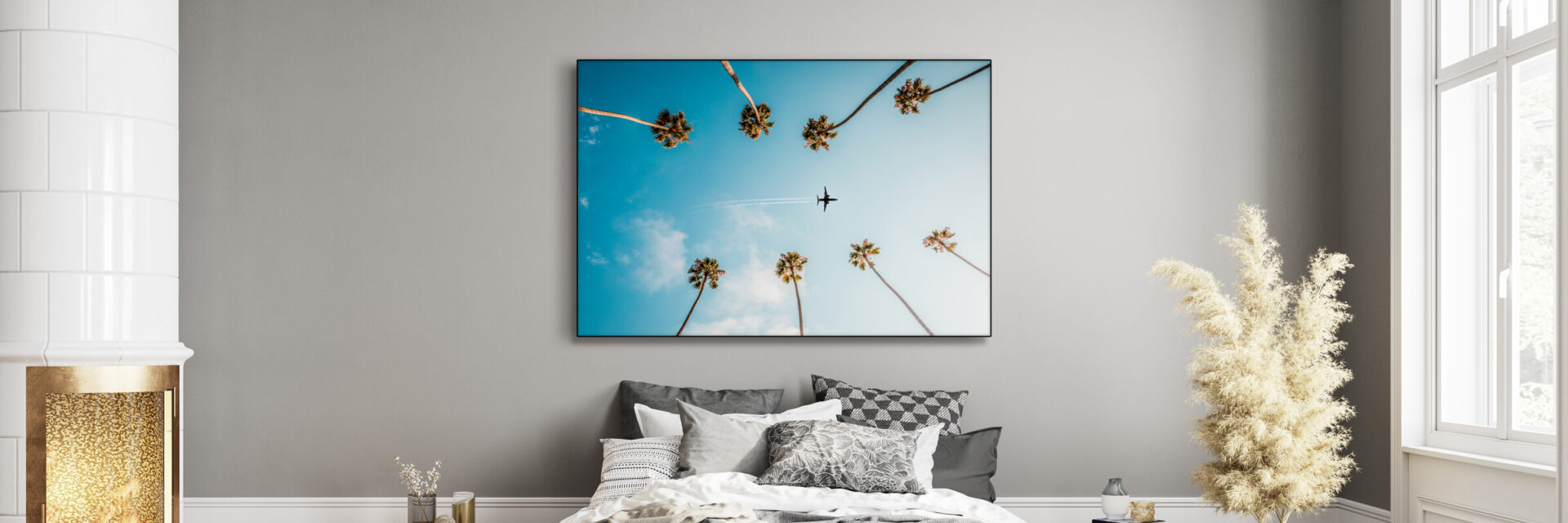Photo featuring plane flying between palm trees through blue skies hangs above bed in bedroom decorated in neutral and grey.