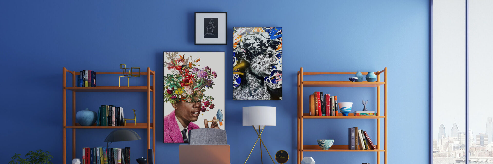 A bold and eclectic maximalist gallery wall is displayed in an office, featuring three large pieces of art hung on a bright blue wall. The art is complemented by decorative wooden shelves adorned with books and small trinkets, creating a unique and personalized aesthetic.