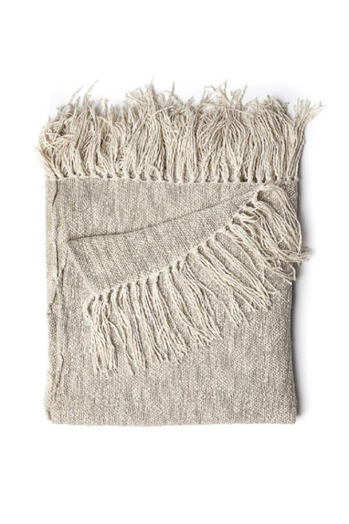 Lightweight woven blanket in neutral tones draped over a sofa in a modern coastal living room.