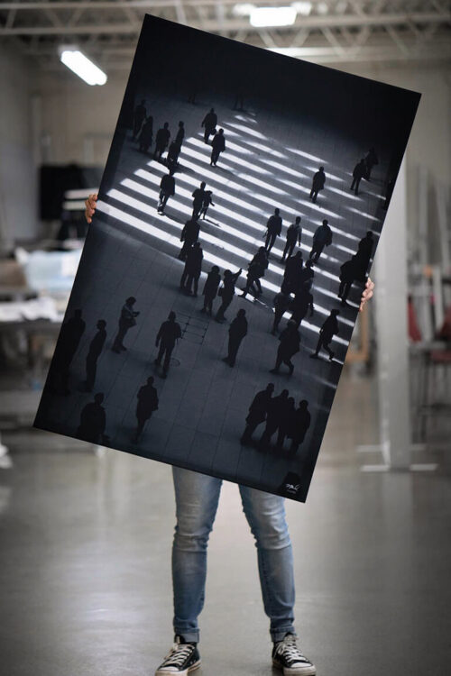Massive black and white aerial photo of sidewalk in NYC is held by a person wearing jeans in a large warehouse.