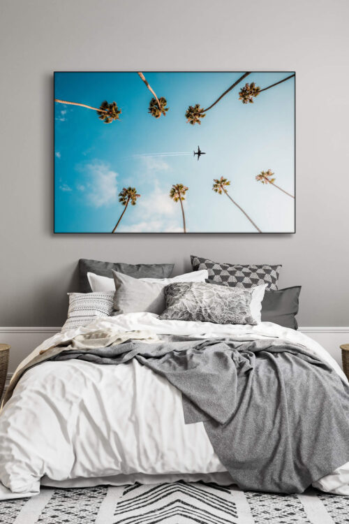Photo featuring plane flying between palm trees through blue skies hangs above bed in bedroom decorated in neutral and grey.