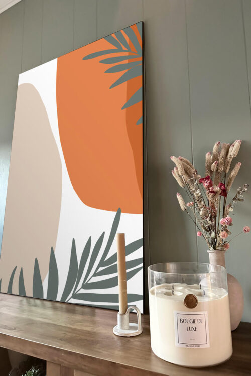 Large orange abstract wall art leans on sage green wall in boho dining room next to sea salt and orchid scented big ass candle and dried floral bouquet.