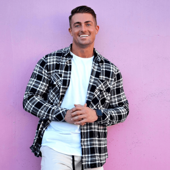 James Bonsall leaned up against a pink wall smiling at the camera