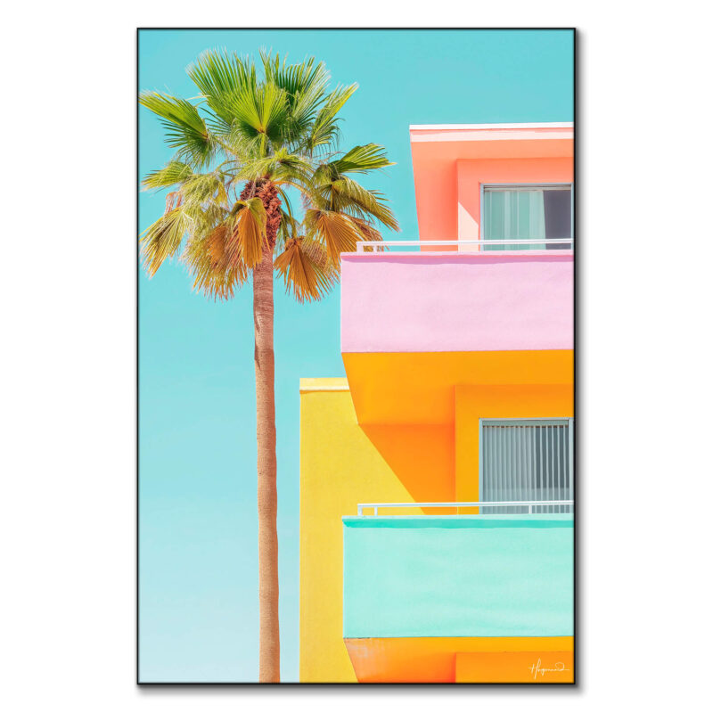 Vibrant modern building with pink, yellow, and turquoise colors, complemented by a tall palm tree, against a clear blue sky.